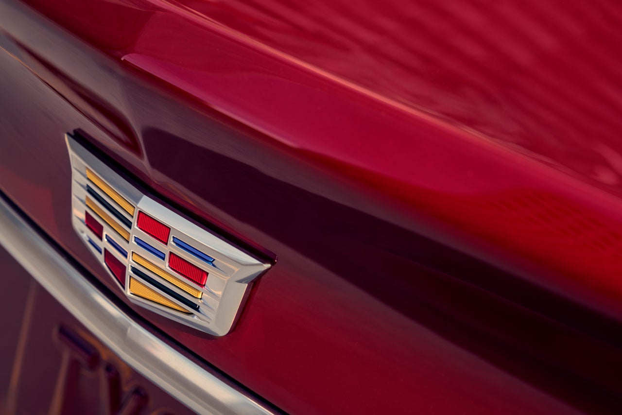 Close-up of a Cadillac emblem on a red car, showing the colorful crest shield with gold, blue, and red bars.